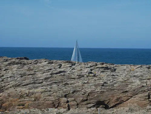 Voile d'un bateau dépasse de derriere les rochers sur la côte de l'océan atlantique