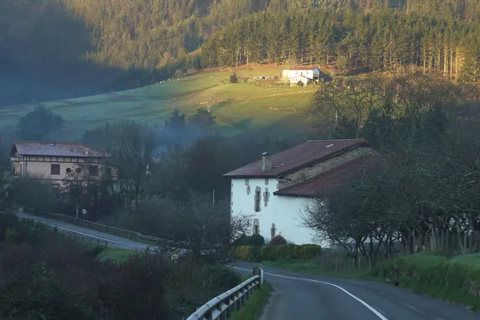 Vue sur une vallée au petit matin avec la rosée et le soleil qui pointe sur le haut éclairant une maison blanche